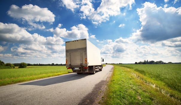 asphalt road on dandelion field with a small truck. lorry moving on sunny evening