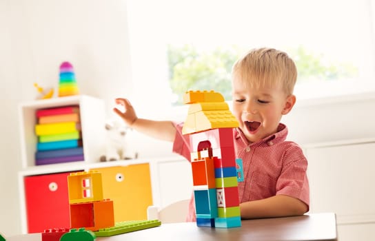 Little child playing with blocks. Boy sitting on the chair at table and building a house