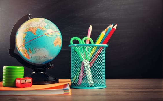 school accessories on the table with blackboard background. Pencils and globe