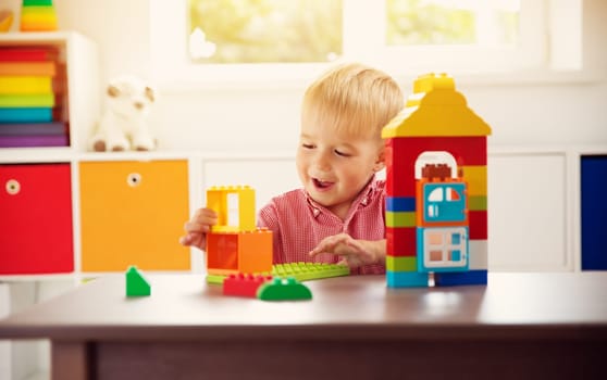 Little child playing with blocks. Boy sitting on the chair at table and building a house