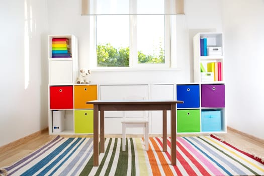 Colourful children rooom with white walls and furniture. Rainbow carpet at home interior with a window