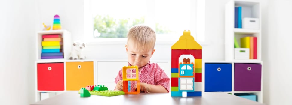 Little child playing with blocks. Boy sitting on the chair at table and building a house