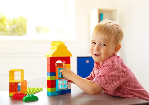 Little child playing with blocks. Boy sitting on the chair at table and building a house