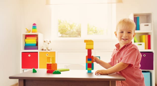 Little child playing with blocks. Boy sitting on the chair at table and building a house