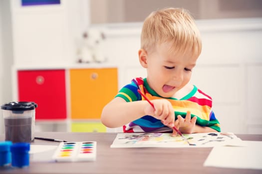 Little child drawing on the paper. Boy sitting on the chair at table with paints