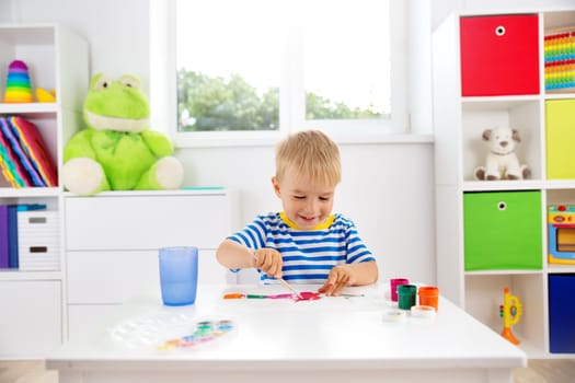 Little child drawing on the paper. Boy sitting on the chair at table with paints