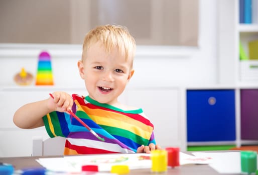 Little child drawing on the paper. Boy sitting on the chair at table with paints
