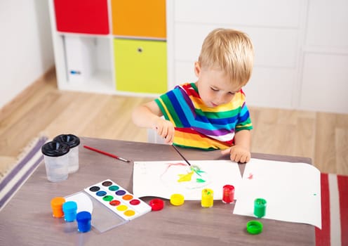 Little child drawing on the paper. Boy sitting on the chair at table with paints