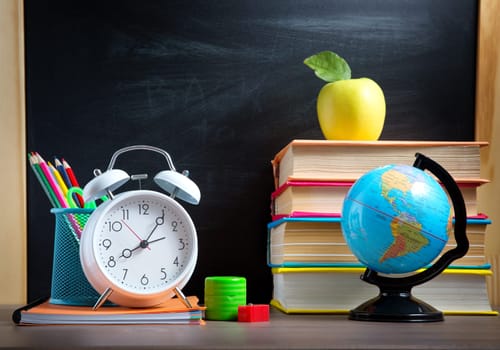 school accessories on the table with blackboard background. Pencils and books