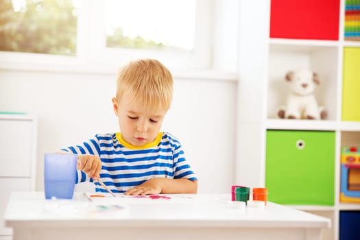 Little child drawing on the paper. Boy sitting on the chair at table with paints