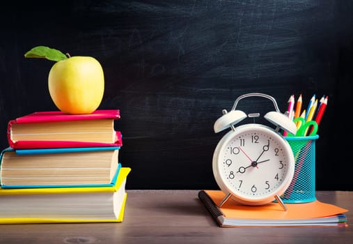 school accessories on the table with blackboard background. Pencils and books