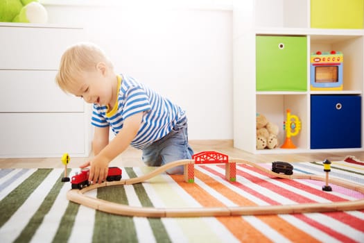 Little child playing with railroad. Boy sitting on the floor at home
