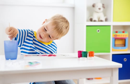 Little child drawing on the paper. Boy sitting on the chair at table with paints