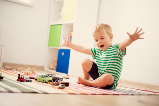 Little child playing with toy cars. Boy sitting on the floor at home