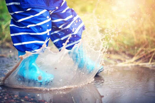 Child walking in wellies in puddle on rainy weather. Boy under rain in summer