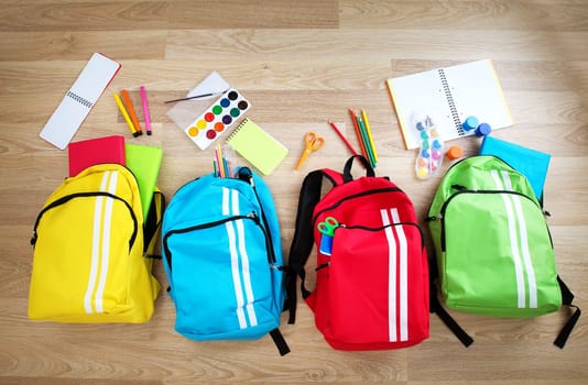Colourful children schoolbags on wooden floor. Backpacks with school accessories