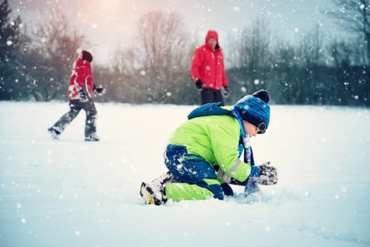 Father with sons walking at snowfall. Children in winter clothes playing with snow and sledding with dad