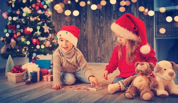 Boy and girl lying on the floor with presents near christmas tree. Children in red hats at home in winter