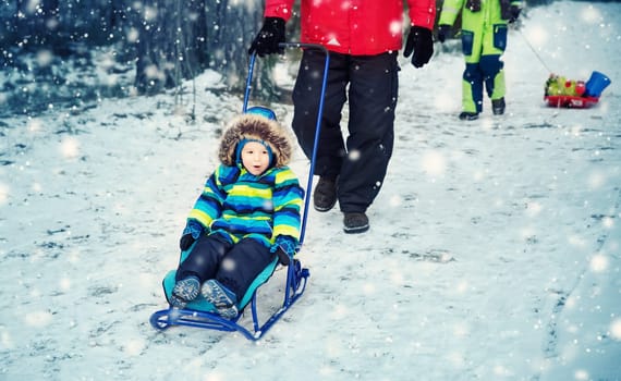 Father with sons walking at snowfall. Children in winter clothes playing with snow and sledding with dad