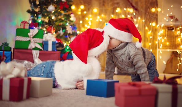 Boy and girl lying on the floor with presents near christmas tree. Children in red hats at home in winter