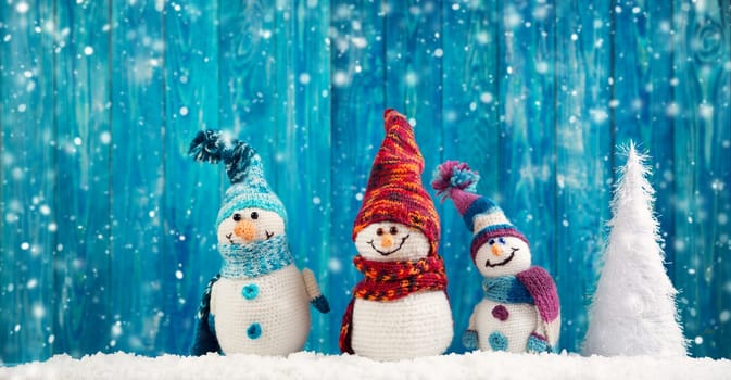 little knitted snowmans on soft snow on blue background