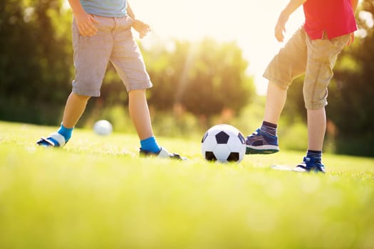 Boys playing football on the field with gates. Active children in summer with ball