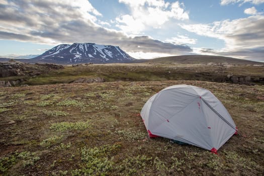 Tent in Icelandic nature with snow covered hill and blue sky with clouds. Concept of adventure on travels in Scandinavian nature. Wide angle of camping in wilderness with copy space.
