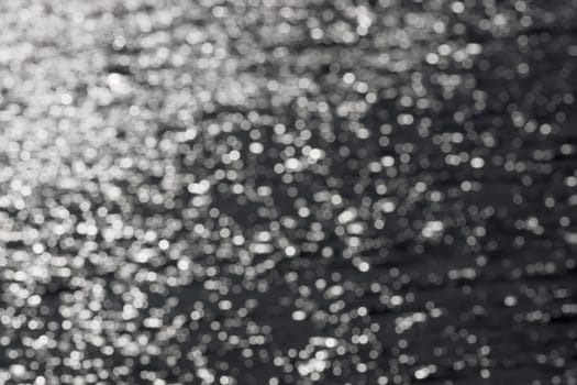 1 - Full frame sparkling out of focus spikes of light, formed from sunlight hitting ripples on a reservoir. monochrome dark grey against white.