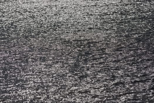 1 - Full frame sunlight shining off surface ripples of large reservoir lake. Glittery shimmer effect. monochrome grey with bright sun flare spots.