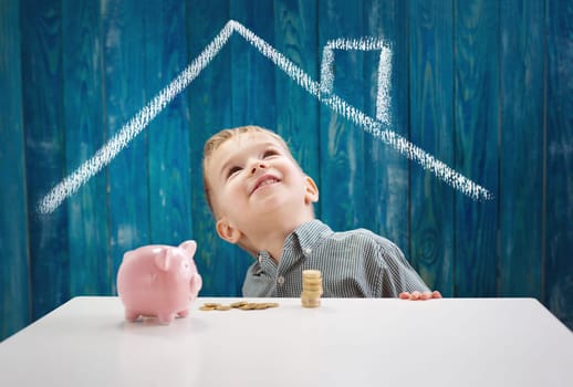 three years old child sitting st the table with money and a piggybank. Happy boy with euro coins. Kid dreaming about home