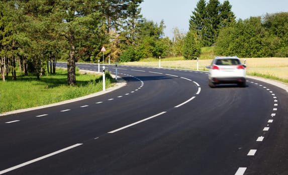 Car on black asphalt road in beautiful spring day at countryside