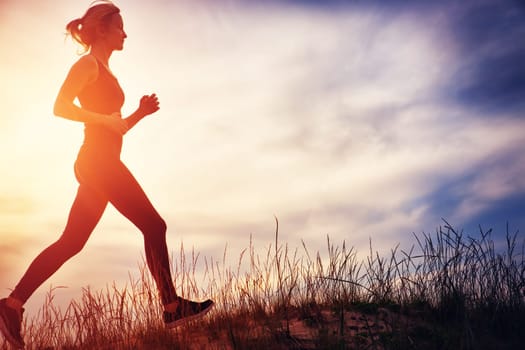 Young woman running on the field near seaside at sunset. Active person outdoors at the dusk in summer