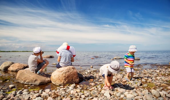 girl and boys standing on the beach in summer hats and holding steering wheel, lifebuoy and binoculars. Children playing at sea in nature