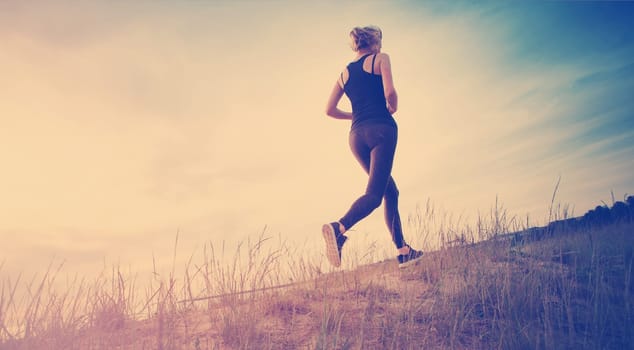 Young woman running on the field near seaside at sunset. Active person outdoors at the dusk in summer
