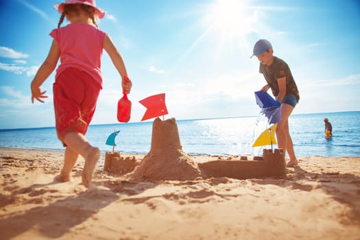 Boy and girl playing on the beach on summer holidays. Children building a sandcastle at sea