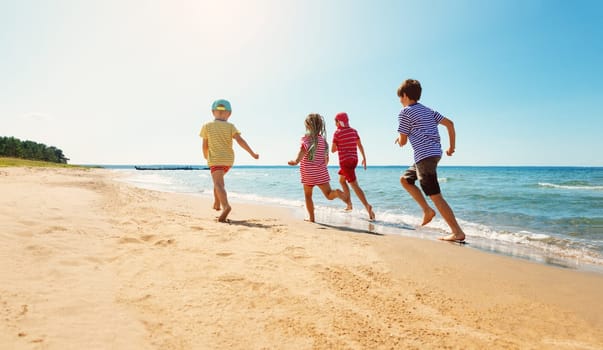 Boys and girl playing on the beach on summer holidays. Children in nature with beautiful sea, sand and blue sky. Happy kids on vacations at seaside running near the water