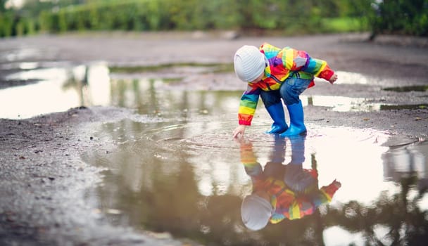 Child walking in wellies and jumping in puddle on rainy weather. Boy under rain in summer outdoors