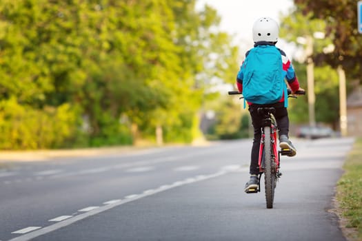 Child with rucksack riding on bikes in the park near school. Pupil with backpack outdoors