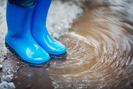 Child walking in wellies in puddle on rainy weather. Boy under rain in summer