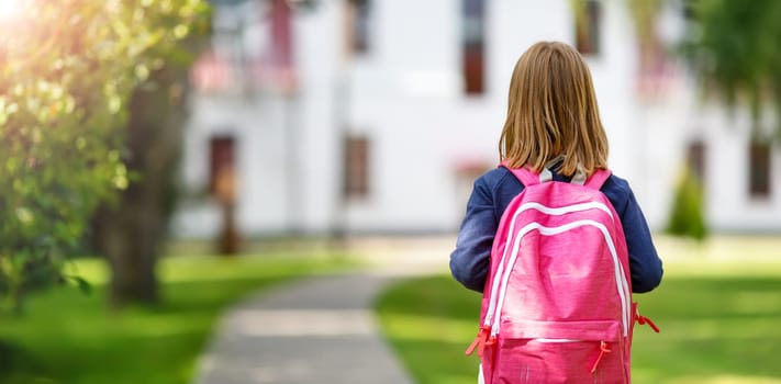 Girl with rucksack infront of a school building. Child with a backpack