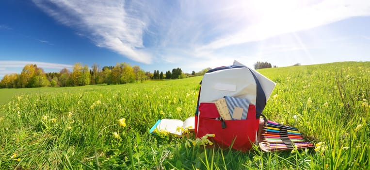 Colourful children schoolbag outdoors on the field. Backpack with school accessories