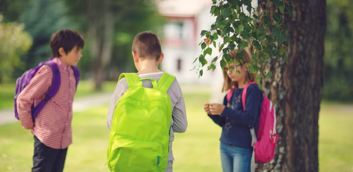 Children with rucksacks standing in the park near school. Pupils with books and backpacks outdoors
