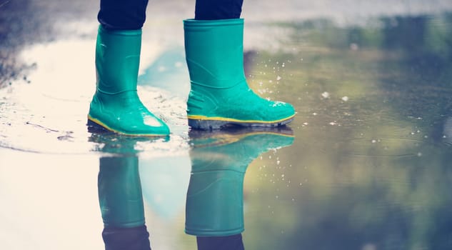 Child walking in wellies in puddle on rainy weather. Boy under rain in summer