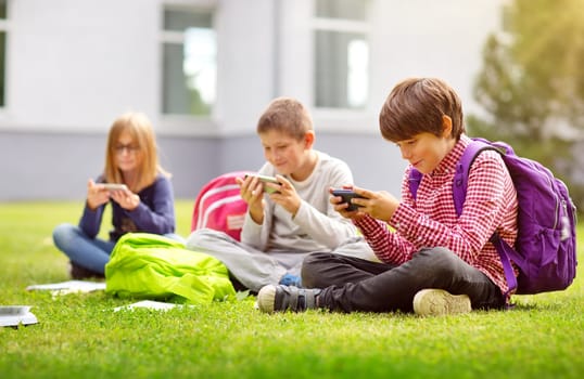 Children with rucksacks sitting in the park near school. Pupils with books and backpacks outdoors