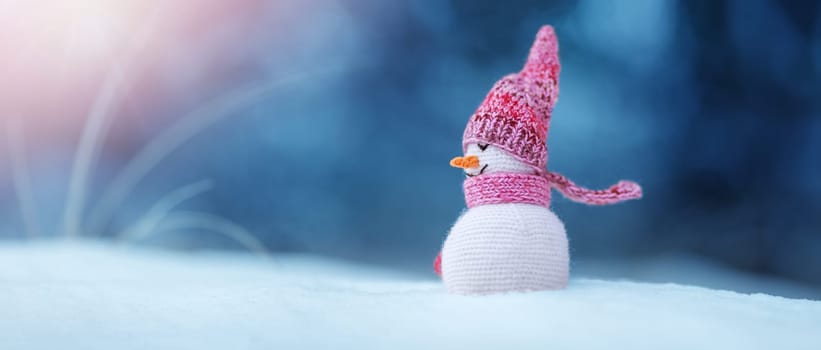 little knitted snowman on soft snow on blue background