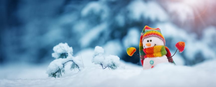 little knitted snowman on soft snow on blue background