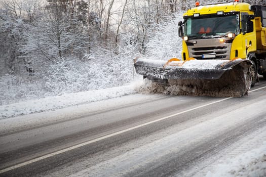 Truck cleaning on winter road covered with snow. Vehicle on snowy alley in the morning at snowfall