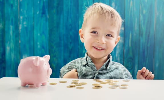 three years old child sitting st the table with money and piggybank. Happy boy with euro coins. Future childhood and education investment. Finance and savings concept