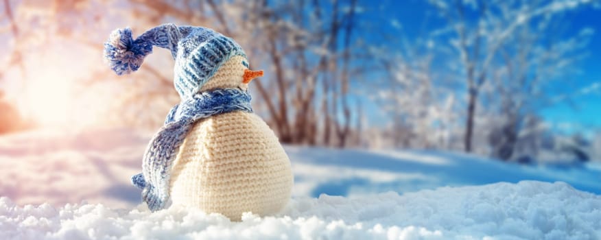 little knitted snowman on soft snow on blue background