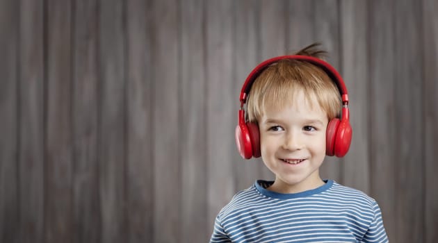 happy little boy on wooden background with red headphones. Child listening music with wireless headset. Musical concept with people
